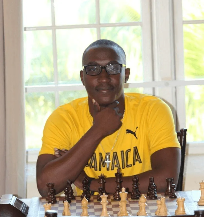 FM Shreyas Smith in a yellow Jamaica shirt behind a chess board